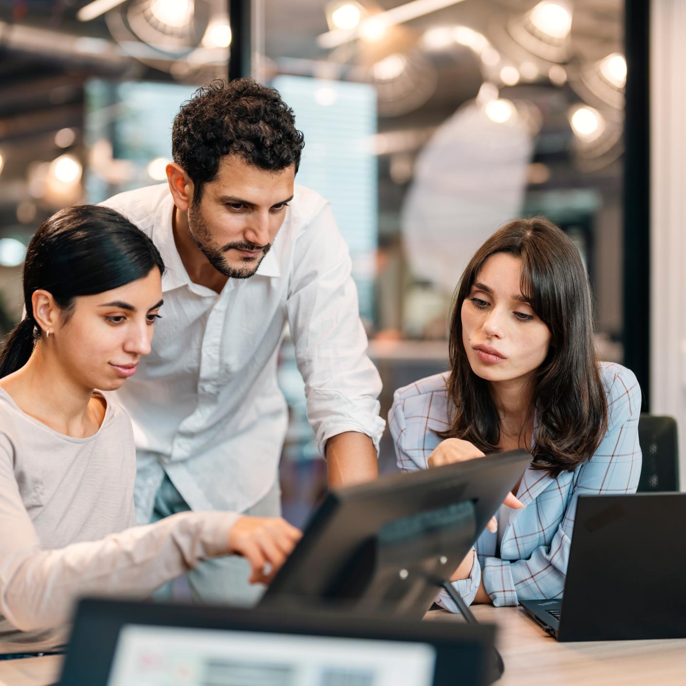 Small group of co-workers working together in a startup business office space. A team of young people in a modern office is discussing their project. Group of business people working. The team are sitting at a board room table looking at a laptop computer