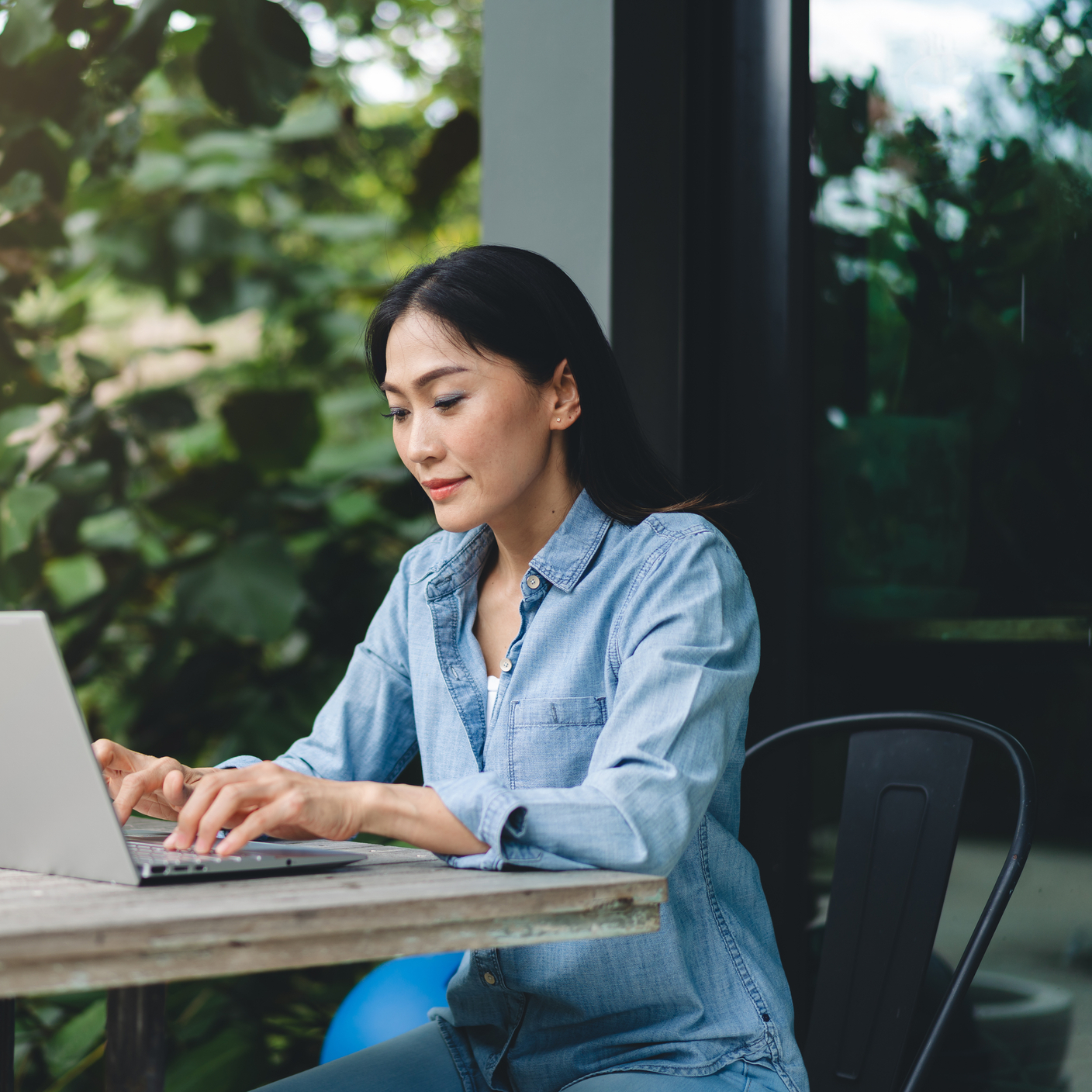 Fröhliche asiatische Frau, die im Freien am Laptop arbeitet; Webkonferenz; Konzept der Telearbeit.
