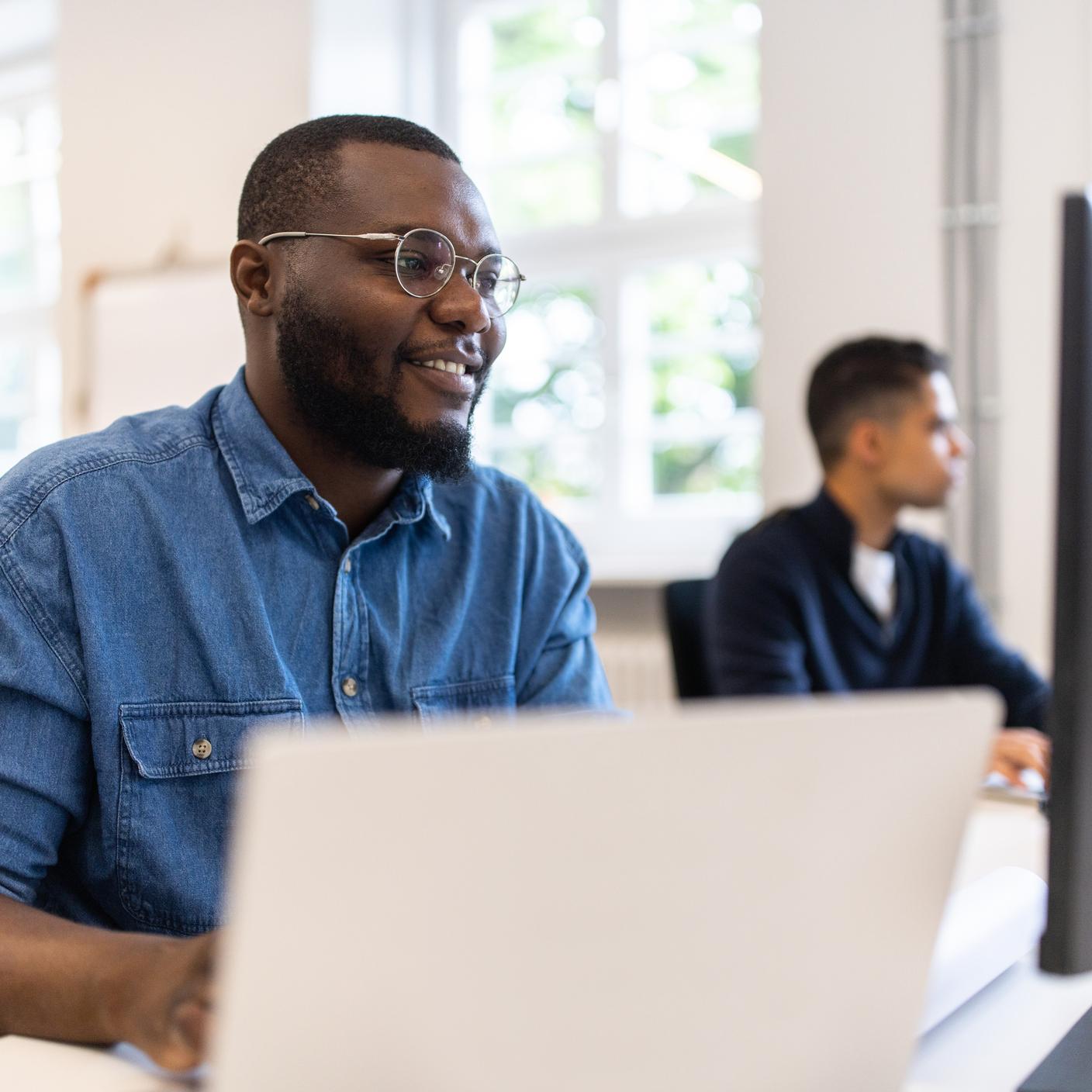Telesoft Technologies a fait des normes la clé de sa stratégie - Homme d’origine africaine heureux travaillant sur un ordinateur de bureau dans un bureau de cotravail