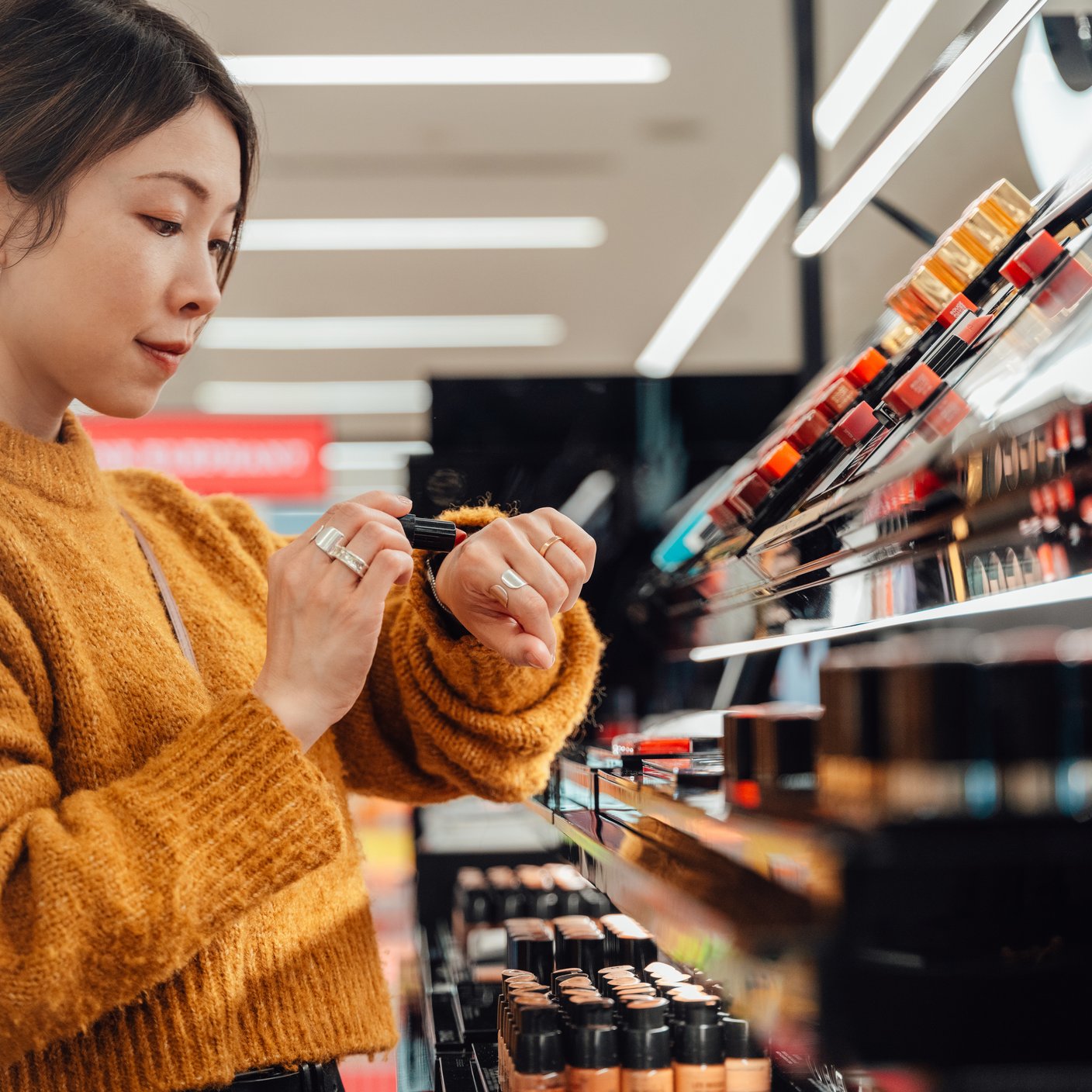 Joven eligiendo tonos de lápiz de labios en el mostrador de cosméticos.