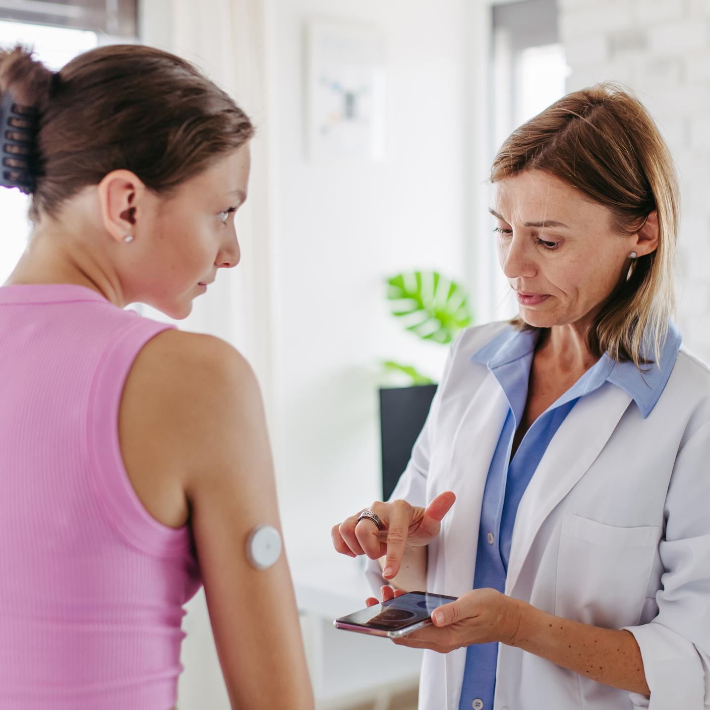 Diabetologist connecting the smartphone to the continuous glucose monitor on a patient's arm