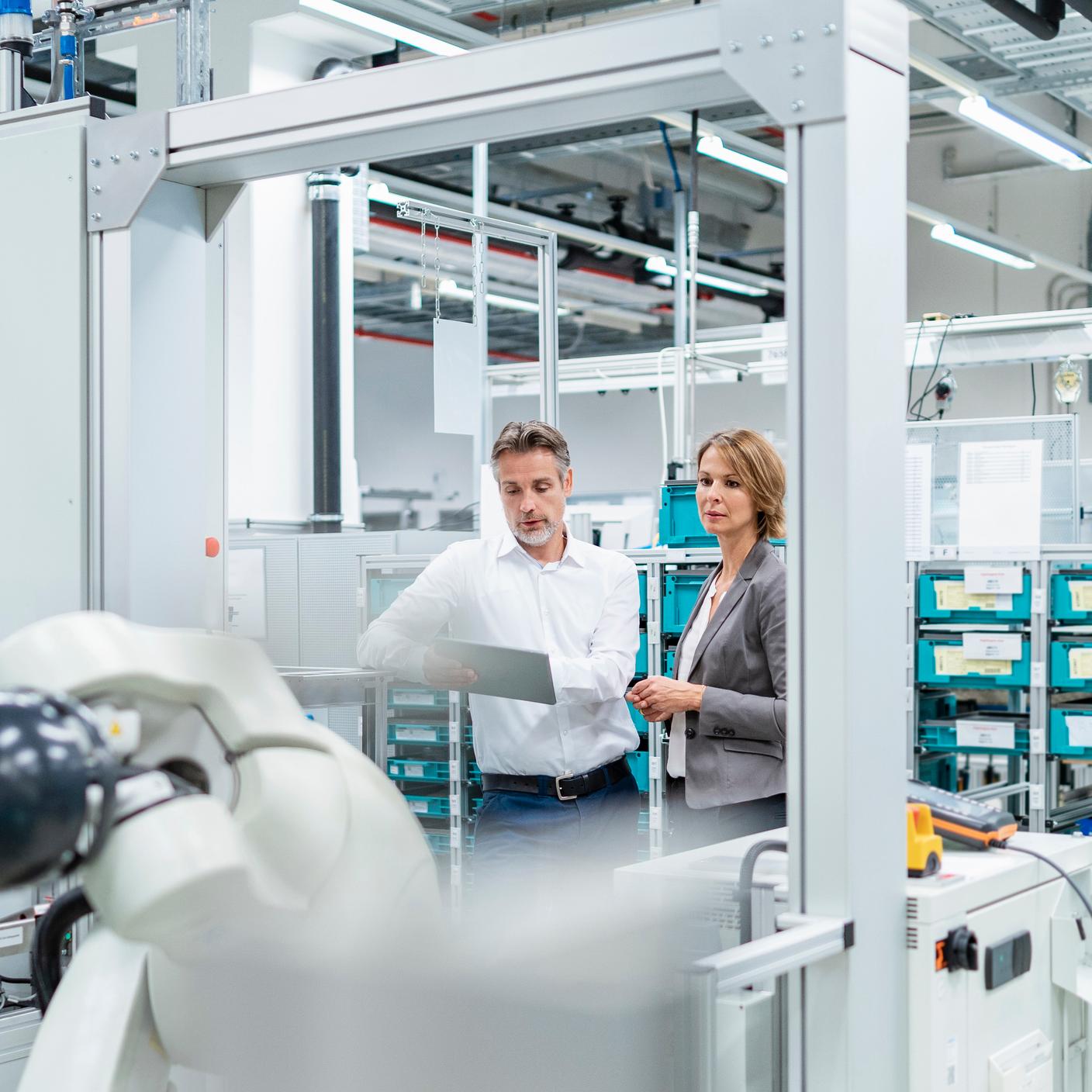 Femme d'affaires et homme tenant une tablette discutant dans une usine moderne