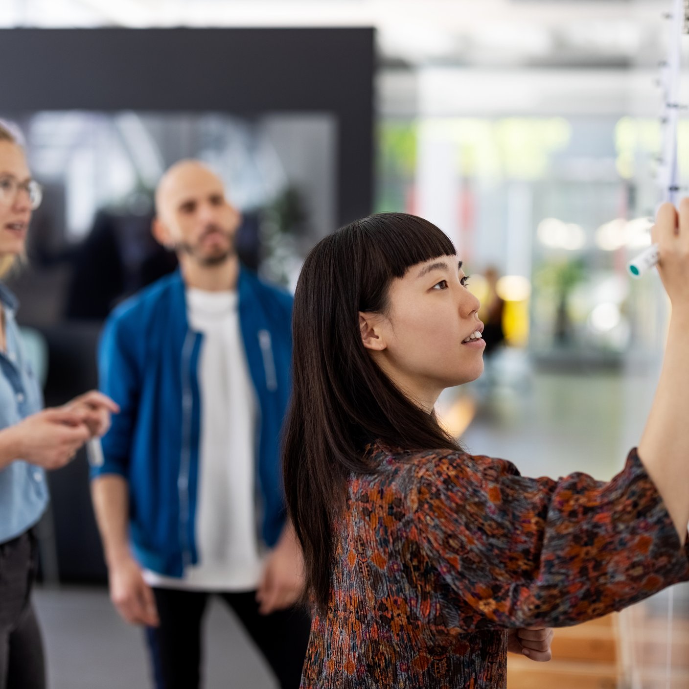 Three professionals in a workshop having a discussion whilst using a whiteboard.