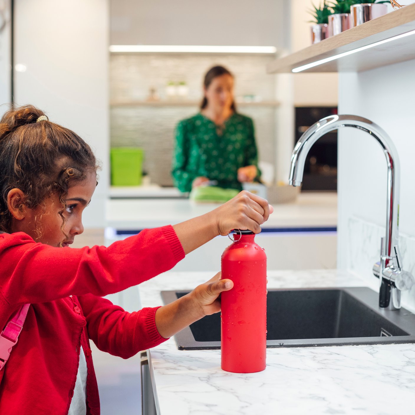 Una joven colegiala con uniforme llena su botella de agua antes de dirigirse a la escuela.