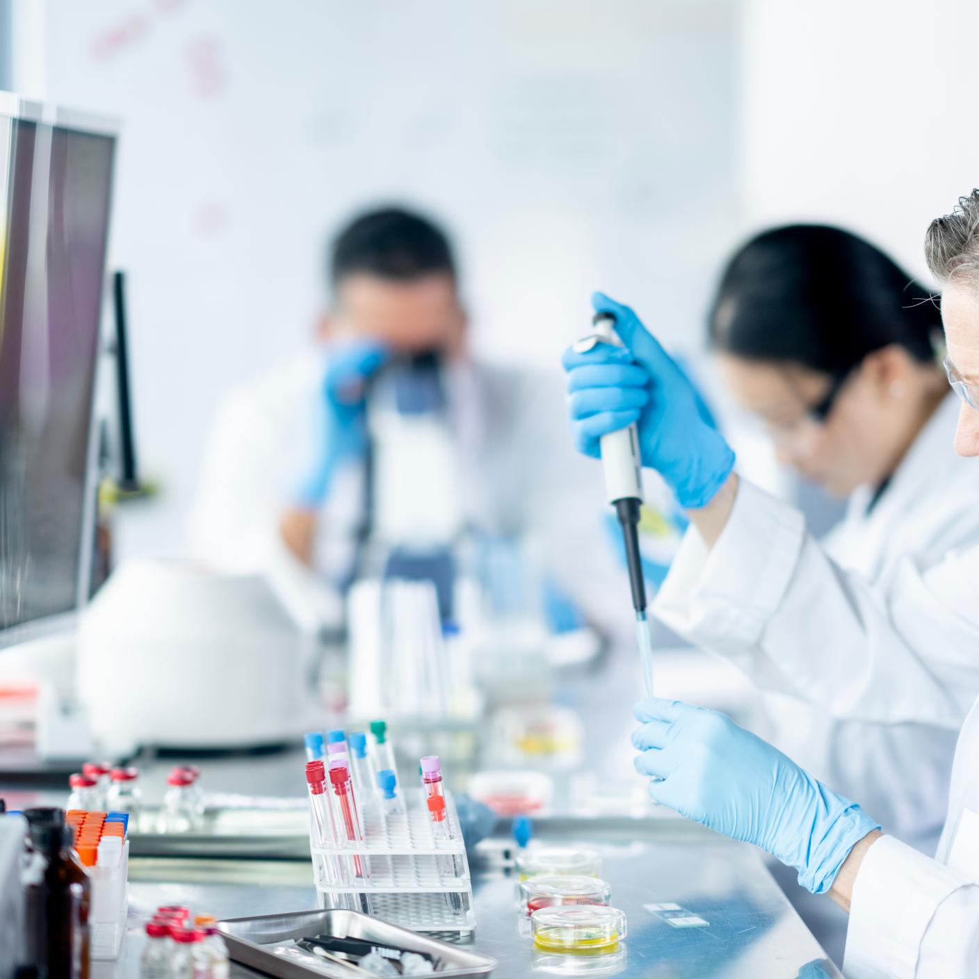 A small team of adults work together in a Medical Lab as they draw samples and take a closer look under microscopes.