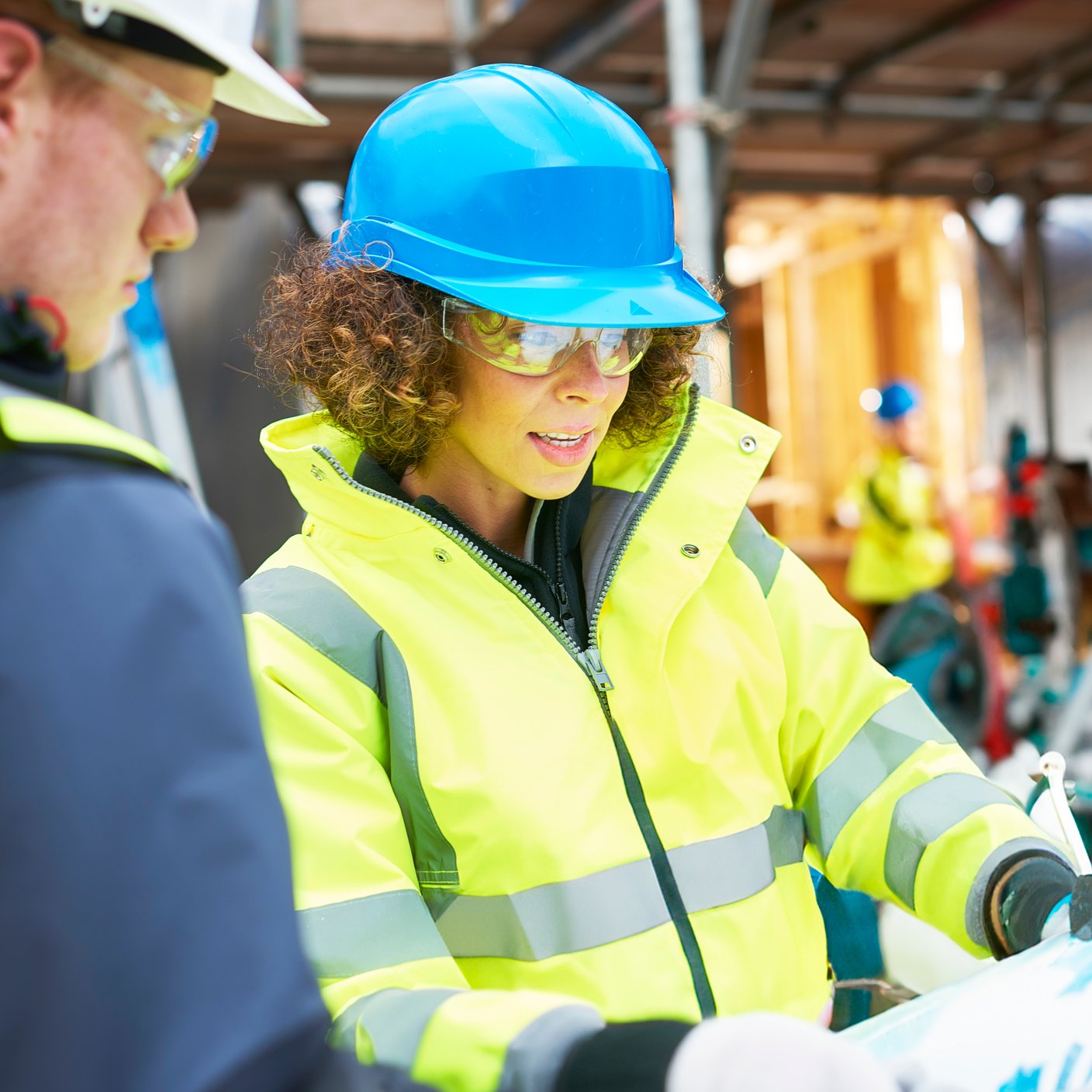 a female construction worker stands on a building site housing development and instructs a co -worker.